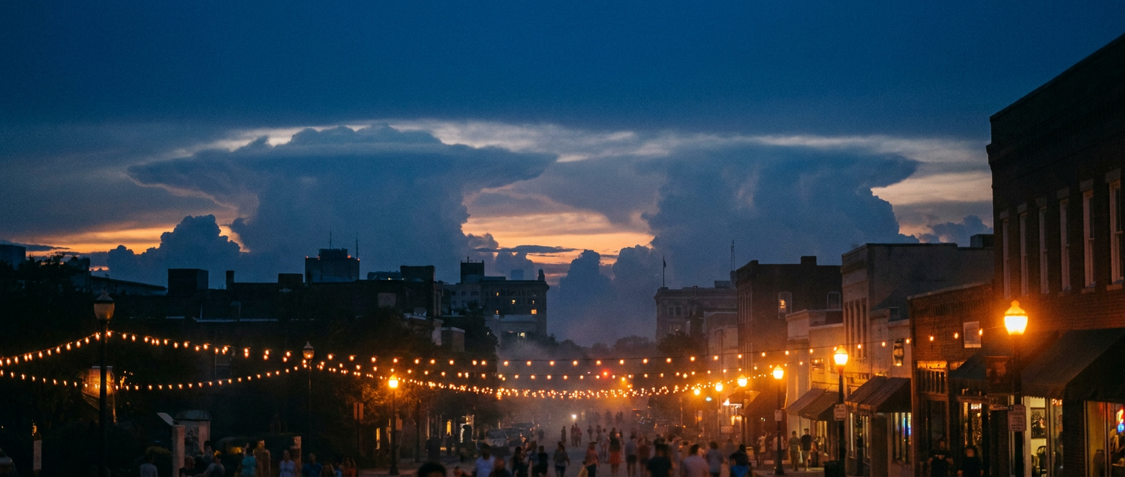 Anvil clouds building over a southern city skyline at dusk, warm humid haze
