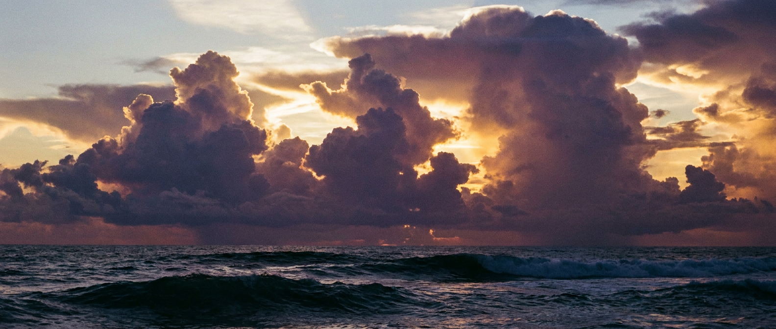 Towering tropical cumulus building over open ocean at dusk, deep purple and gold light