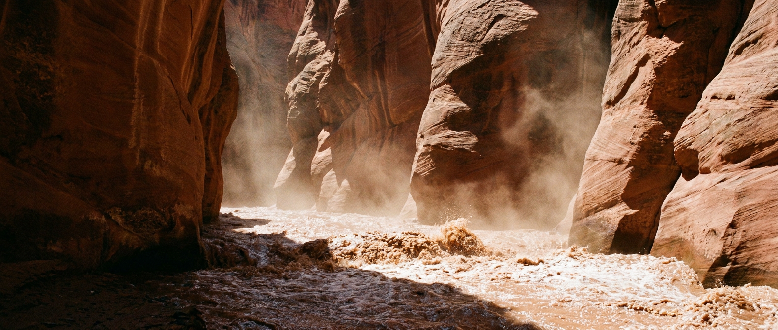 A desert slot canyon filled with fast-moving muddy floodwater, harsh midday sun, red rock walls